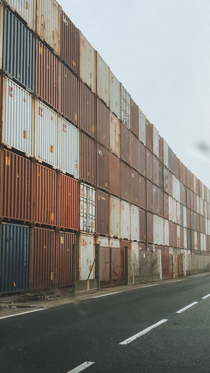 High-rise stack of shipping containers along an industrial road in foggy weather.