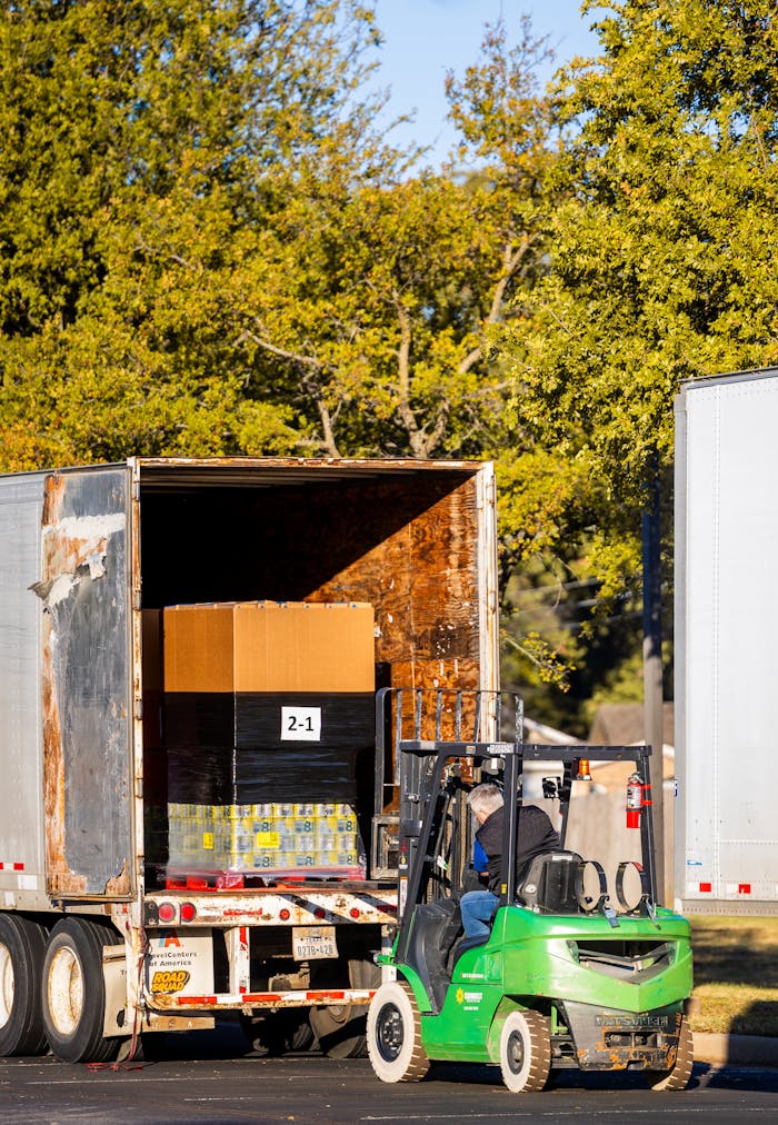 A forklift loading a truck with a pallet in an outdoor setting, surrounded by trees.